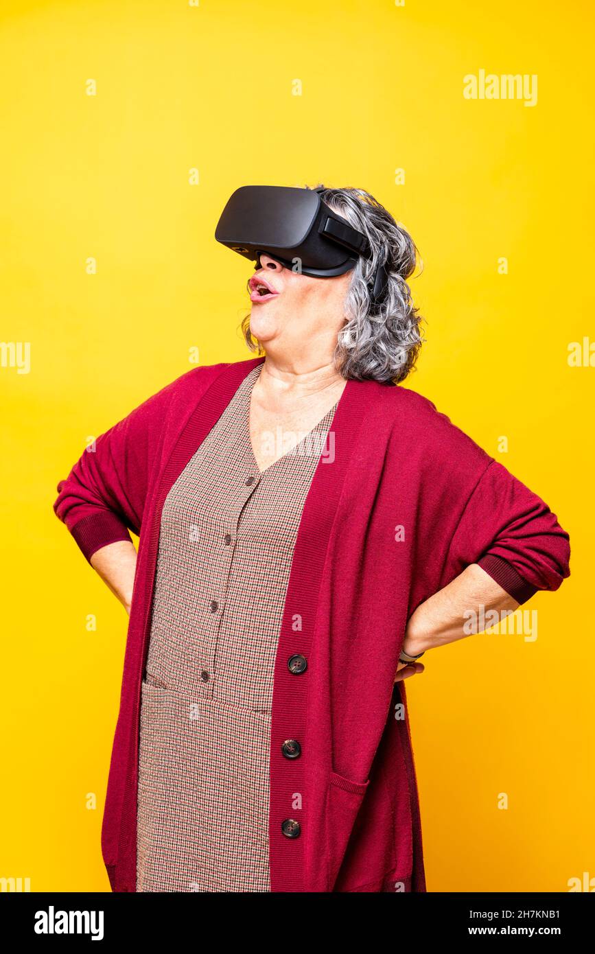 Senior woman laughing while wearing virtual reality headset against yellow background Stock Photo