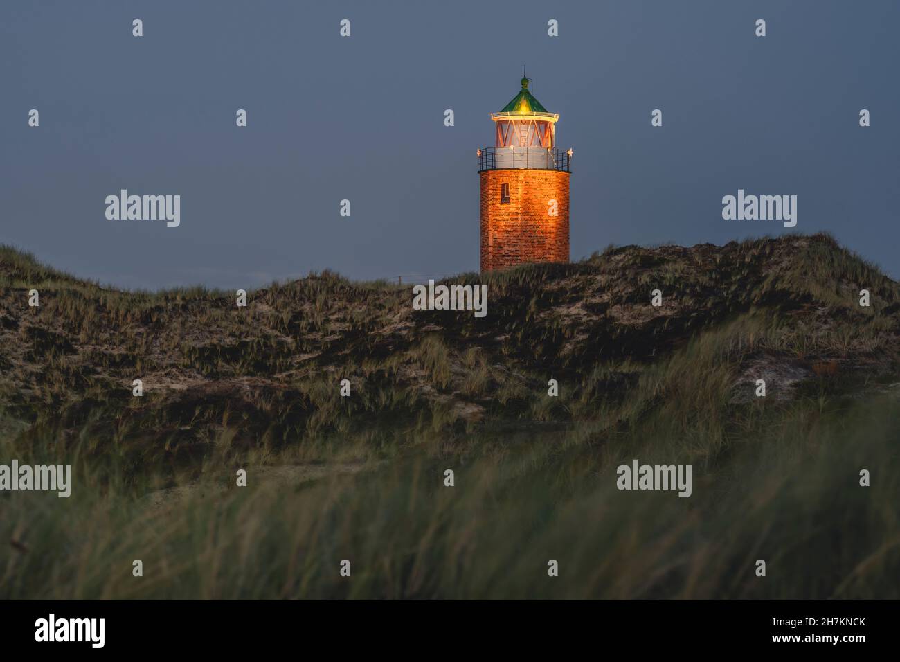 Grassy cliffside with Rotes Kliff Lighthouse in background Stock Photo