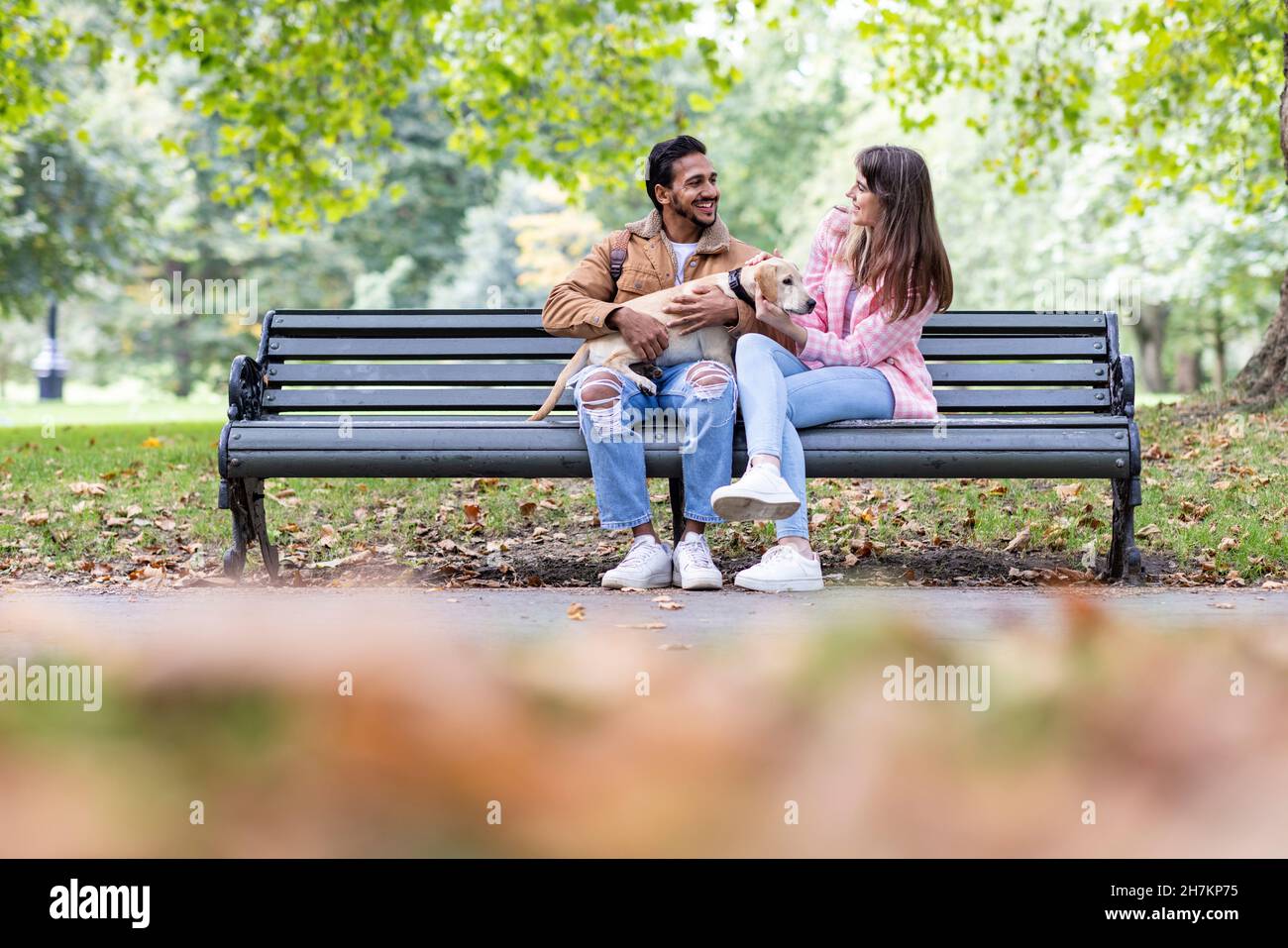 Happy young couple with dog sitting on bench in public park Stock Photo ...