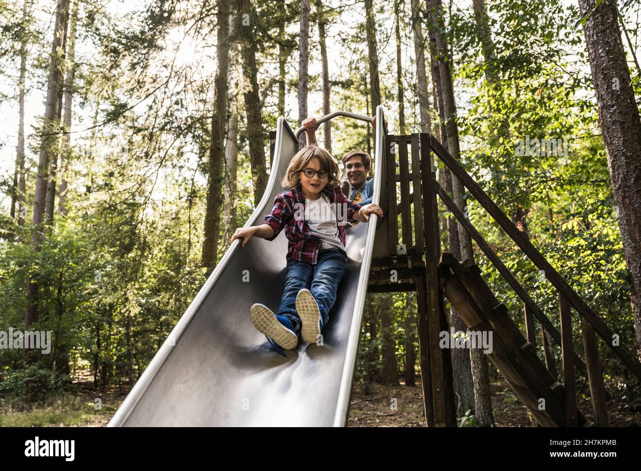 Father and son sliding on slide in forest Stock Photo