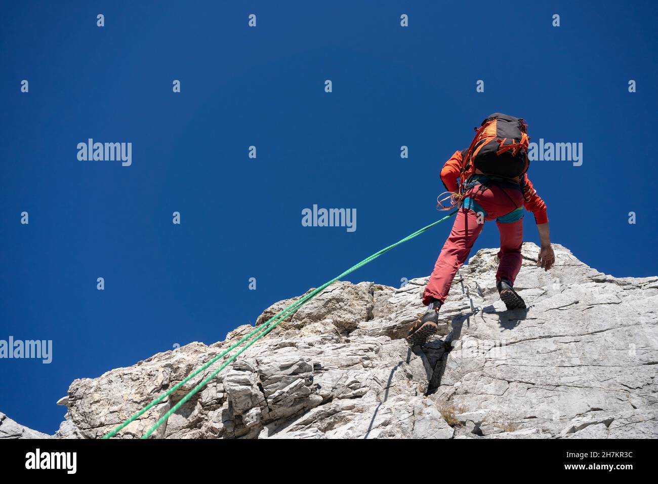 Mature man climbing mountain hill with rope on sunny day Stock Photo