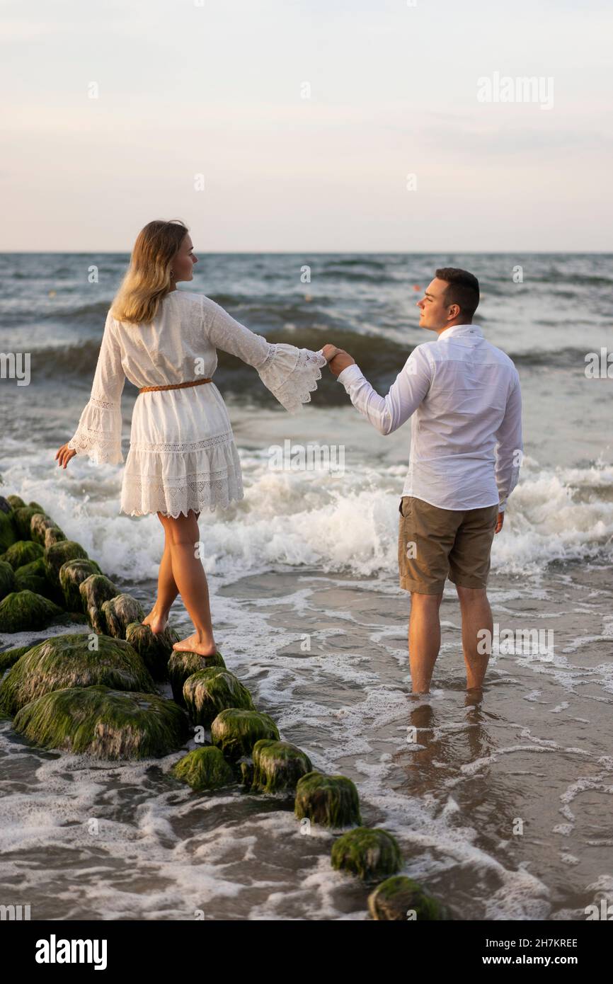 Girlfriend holding hand of boyfriend while walking on rock in sea Stock