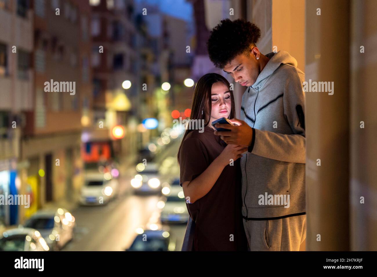 Multi-ethnic couple using smart phone while standing on balcony at night Stock Photo