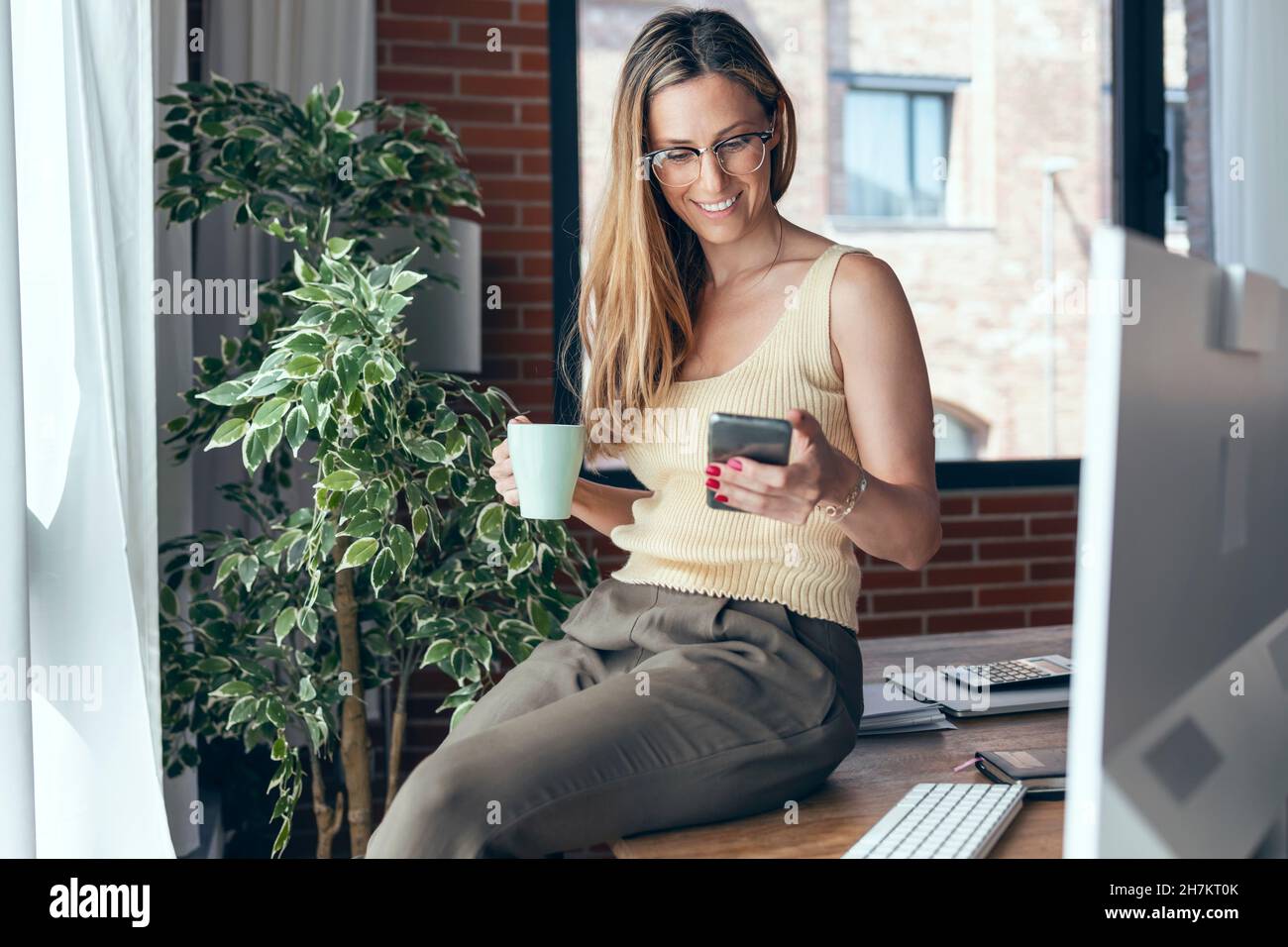 Smiling female freelancer using smart phone while sitting on desk Stock Photo