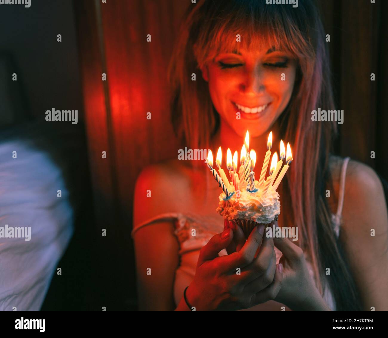 Smiling woman looking at cupcake with burning candles on birthday Stock Photo