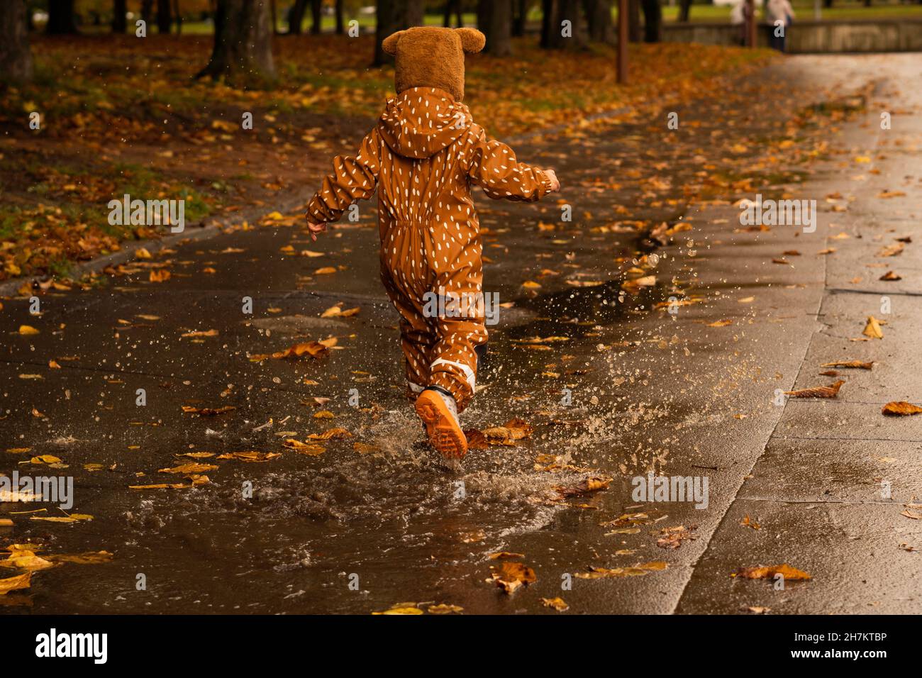 Boy splashing puddle water while running on road Stock Photo