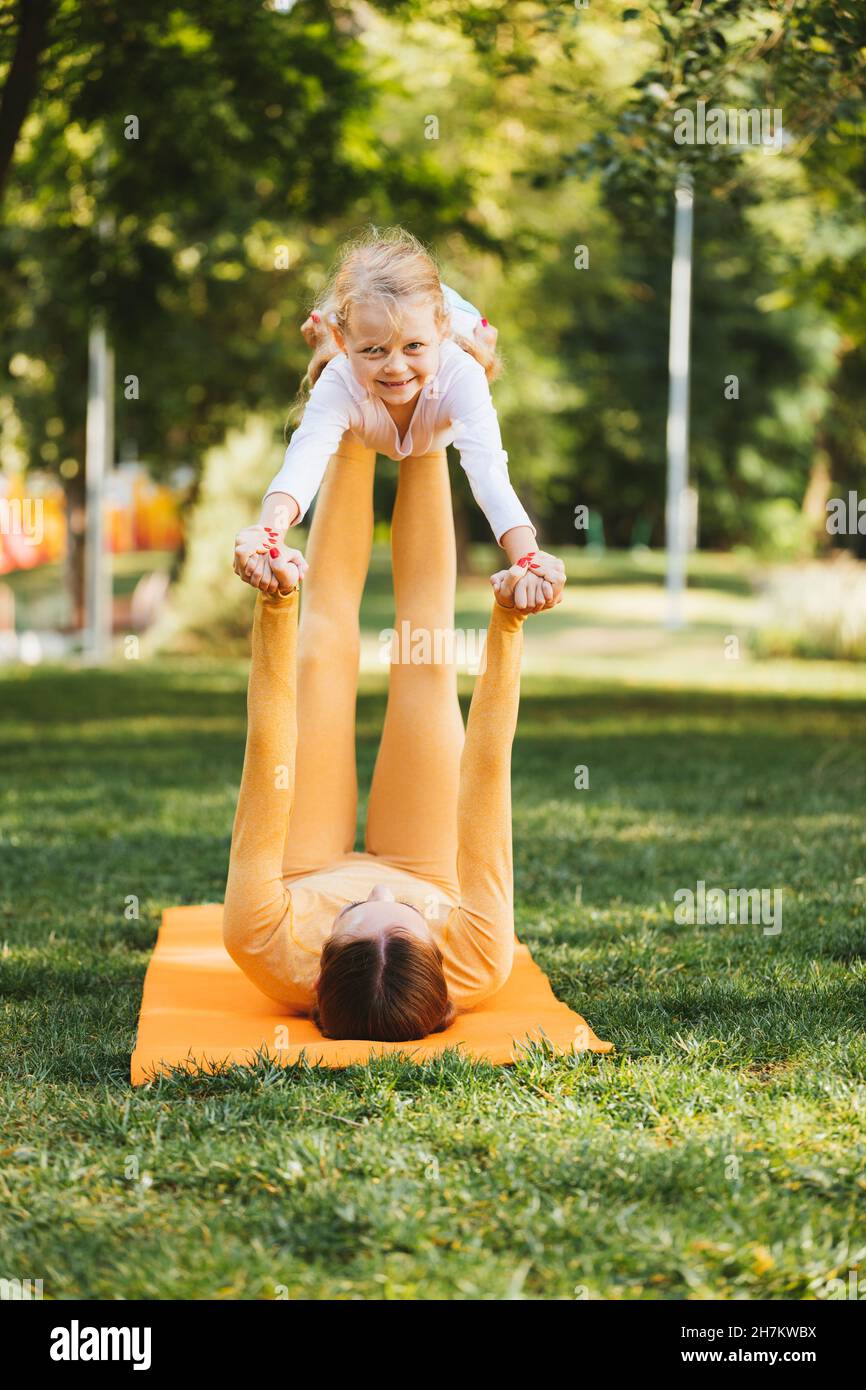 Smiling girl lifted by mother on grass in public park Stock Photo
