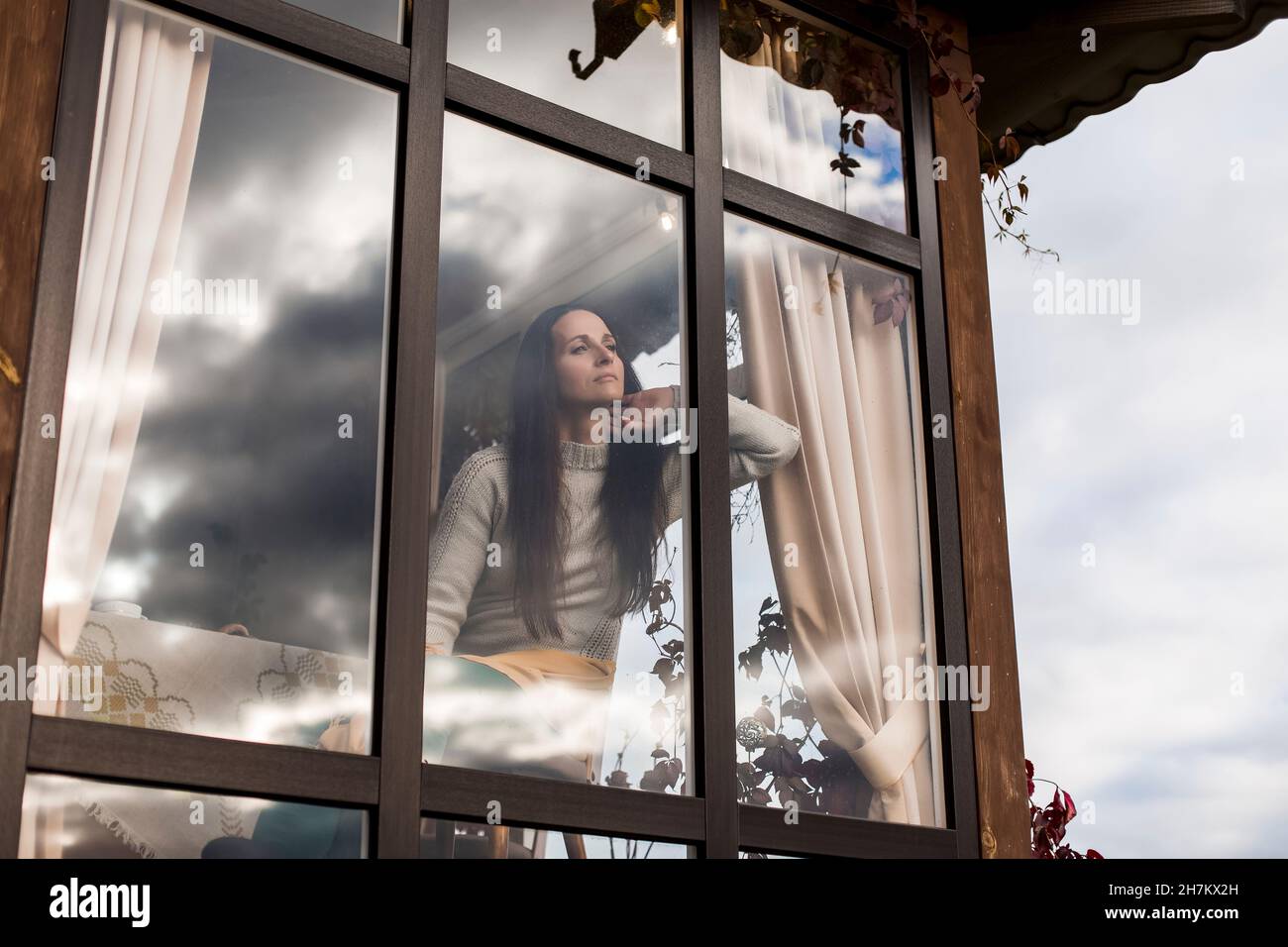 Thoughtful woman looking out of house window Stock Photo