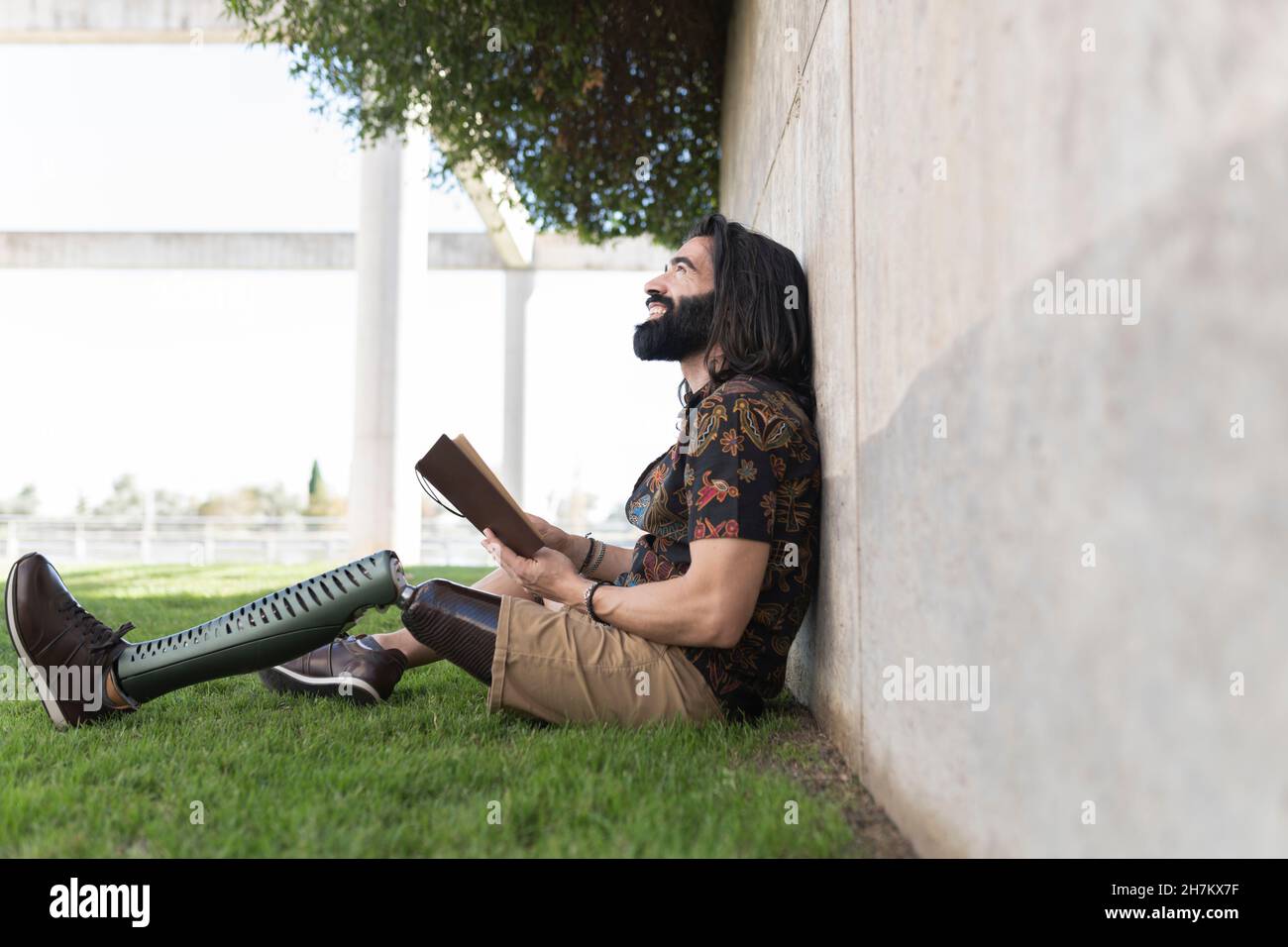 Smiling man with artificial limb reading book in park Stock Photo