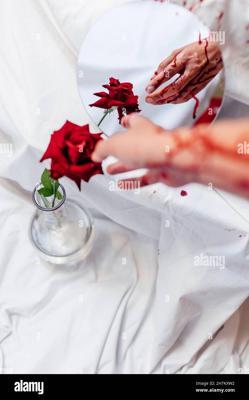 Woman touching rose with bleeding hand by mirror reflection Stock Photo