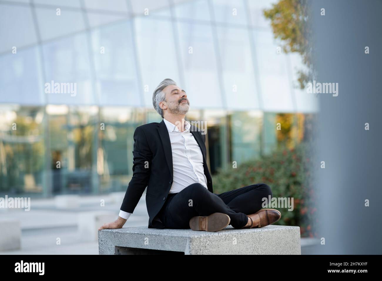 Businessman meditating sitting cross-legged on seat Stock Photo - Alamy