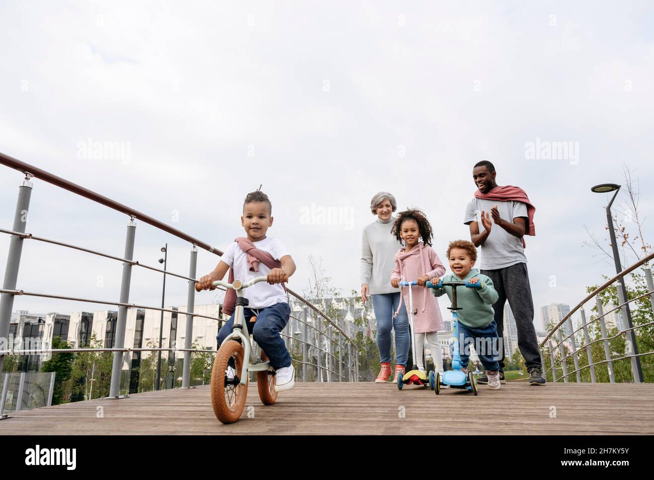 Father cheering for children riding push scooter and bicycle on bridge Stock Photo
