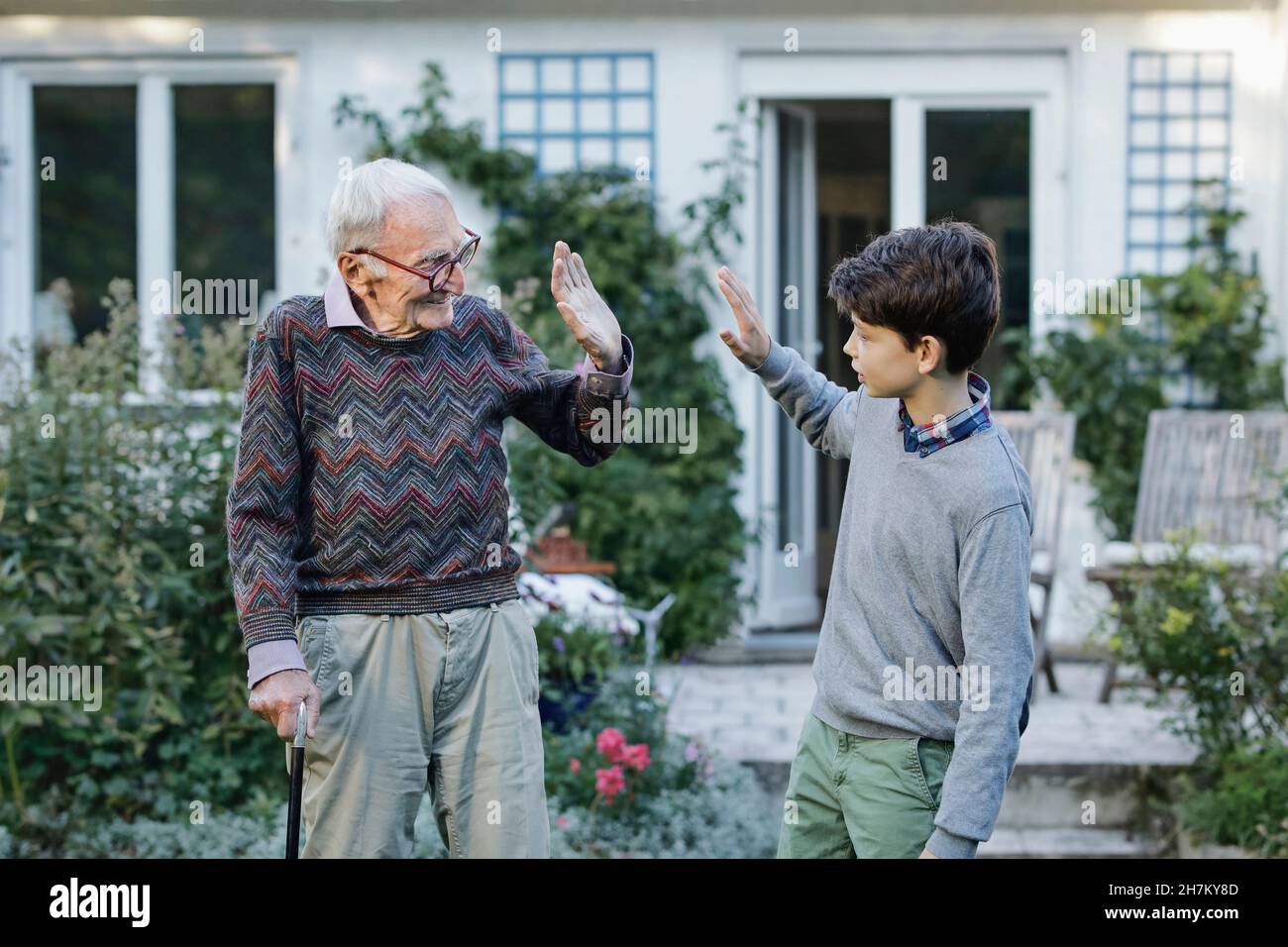 Grandfather giving high-five to grandson in backyard Stock Photo