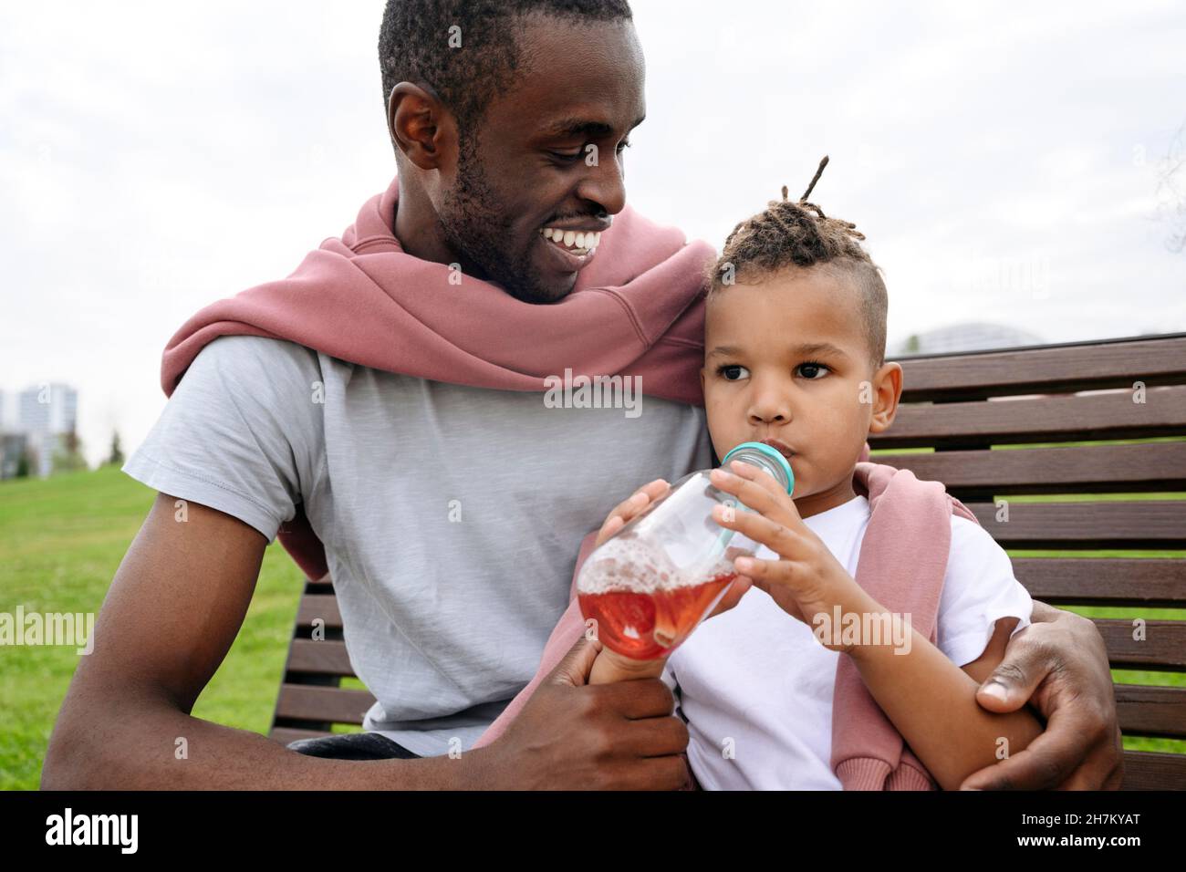 Smiling father looking at boy drinking juice on bench Stock Photo