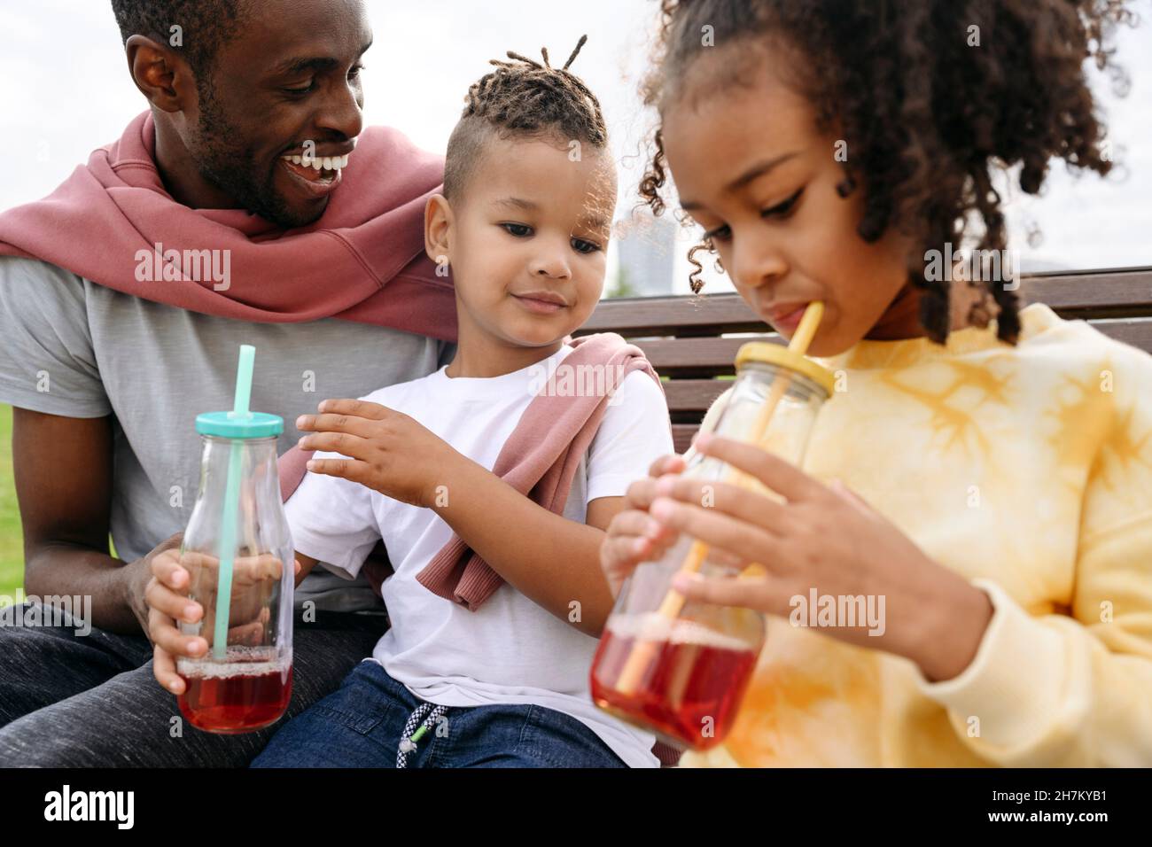 Father looking at children drinking lemonade in park Stock Photo