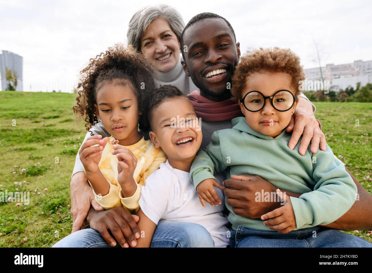 Smiling father sitting with family together on grass Stock Photo - Alamy