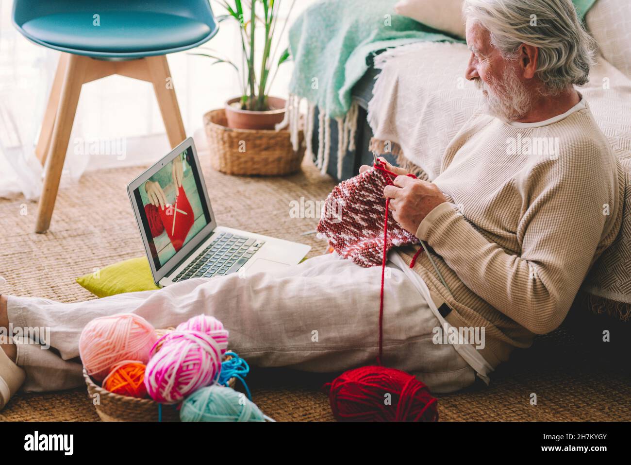 Senior man knitting while watching tutorial through laptop at home Stock Photo