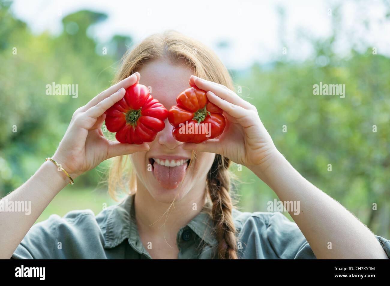 Playful female farmer holding tomatoes in front of eyes and sticking ...