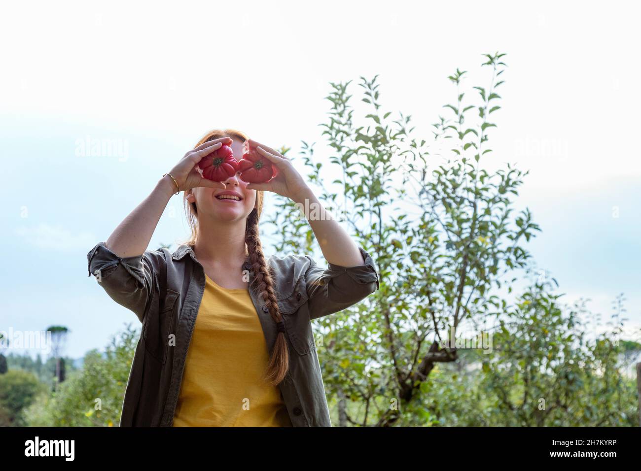 Smiling female farmer holding tomatoes in front of eyes at garden Stock ...