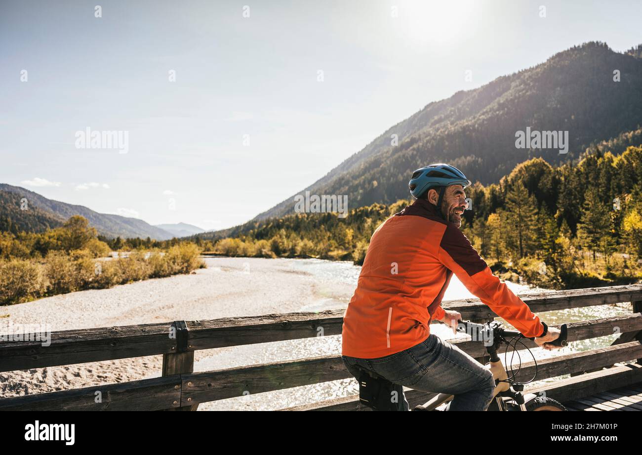 Smiling man with helmet cycling on bridge Stock Photo