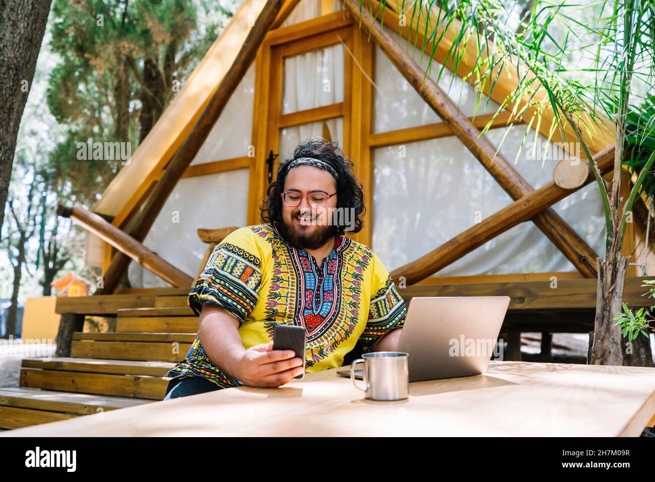 Smiling man with laptop using mobile phone at table Stock Photo