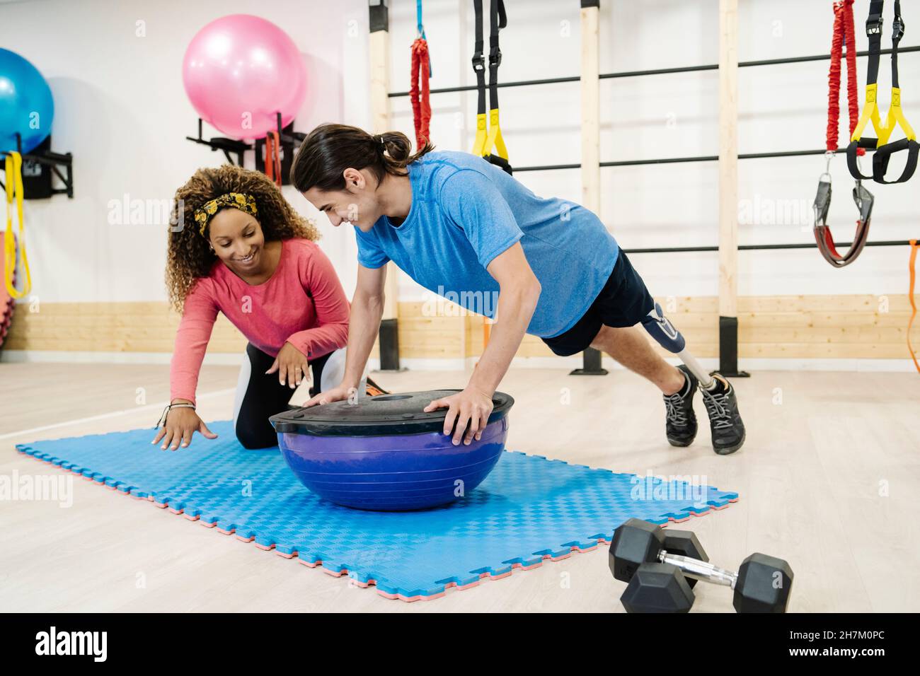 Disabled man with friend exercising on balance ball in gym Stock Photo