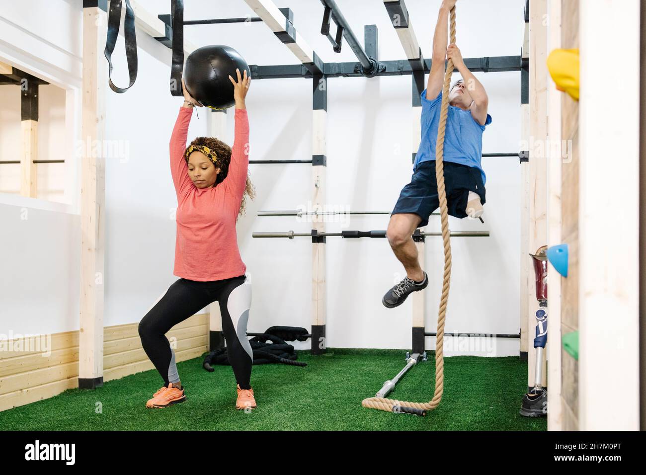 Woman balancing with medicine ball by disabled man climbing rope in gym  Stock Photo - Alamy
