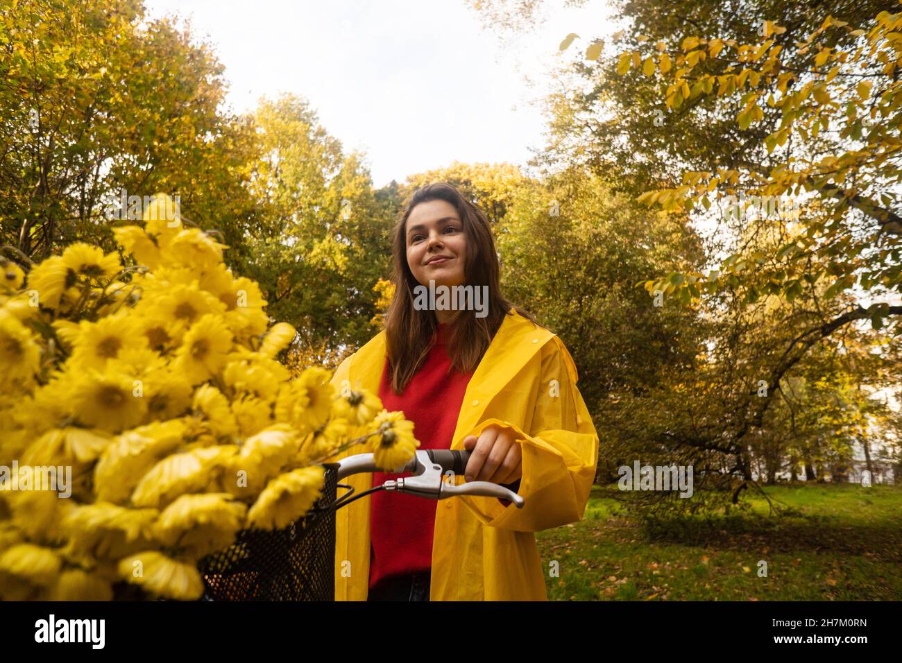 Smiling woman with yellow flowers on bicycle in park Stock Photo