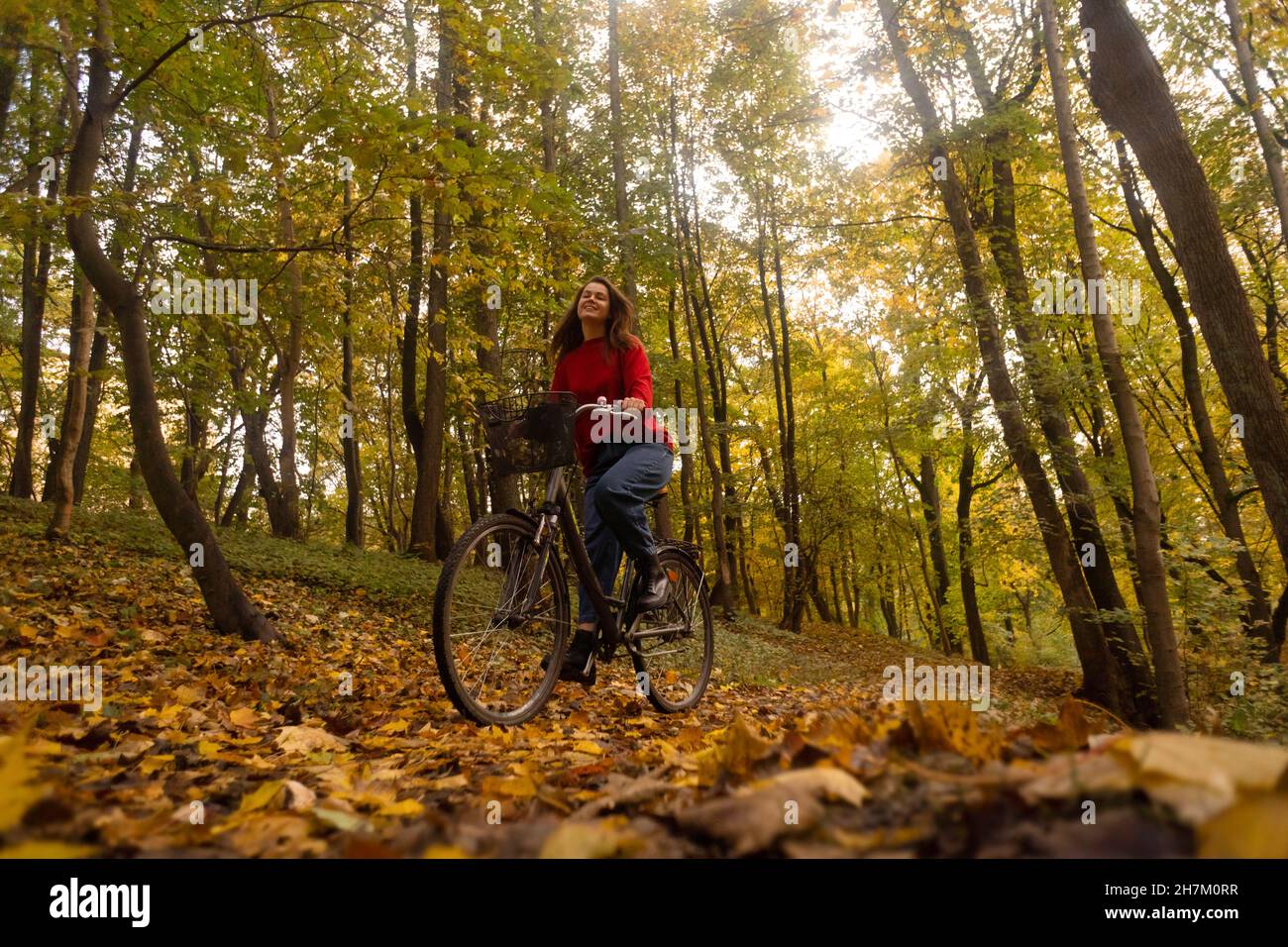 Woman cycling in front of trees at autumn park Stock Photo