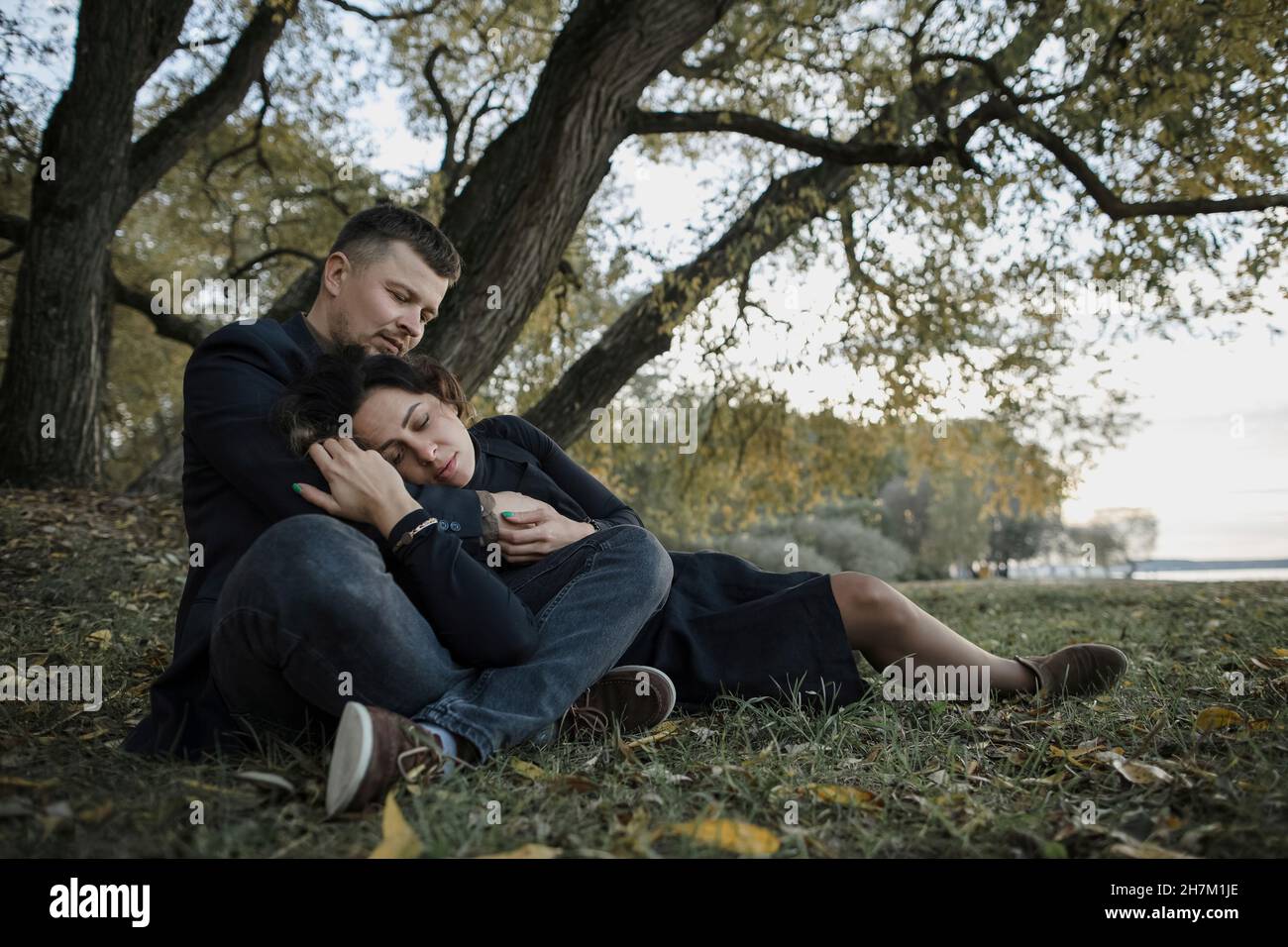 Loving couple relaxing on grass in front of tree Stock Photo - Alamy
