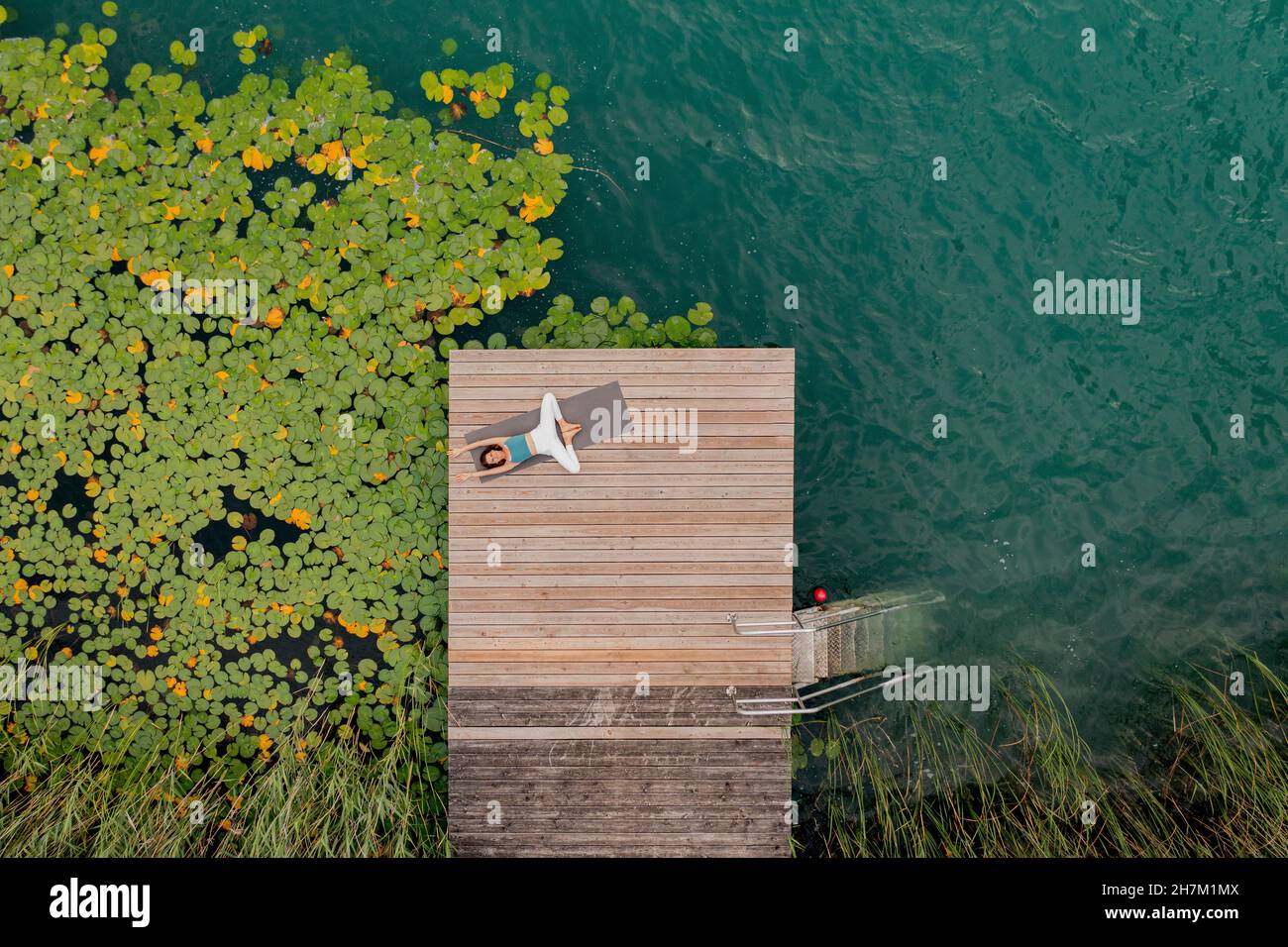 Woman lying on jetty doing yoga by lake Stock Photo