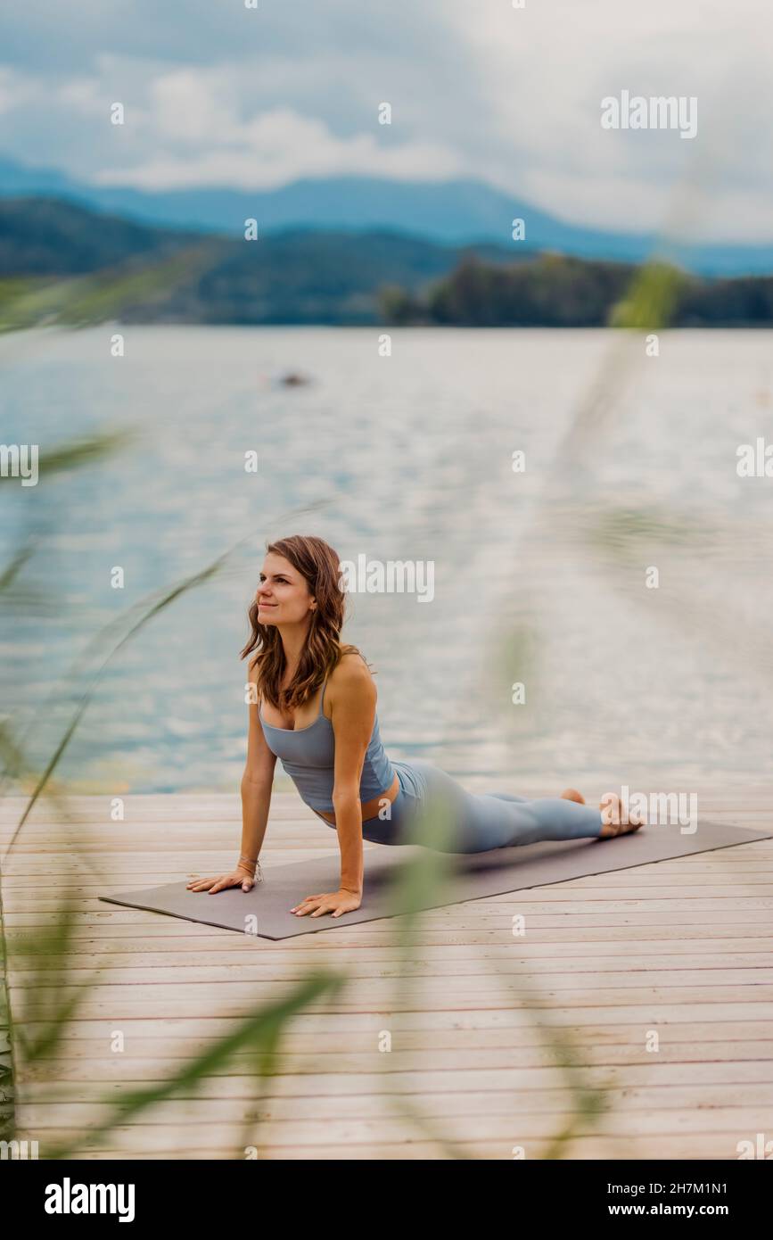 Woman doing push-ups on exercise mat by lake Stock Photo