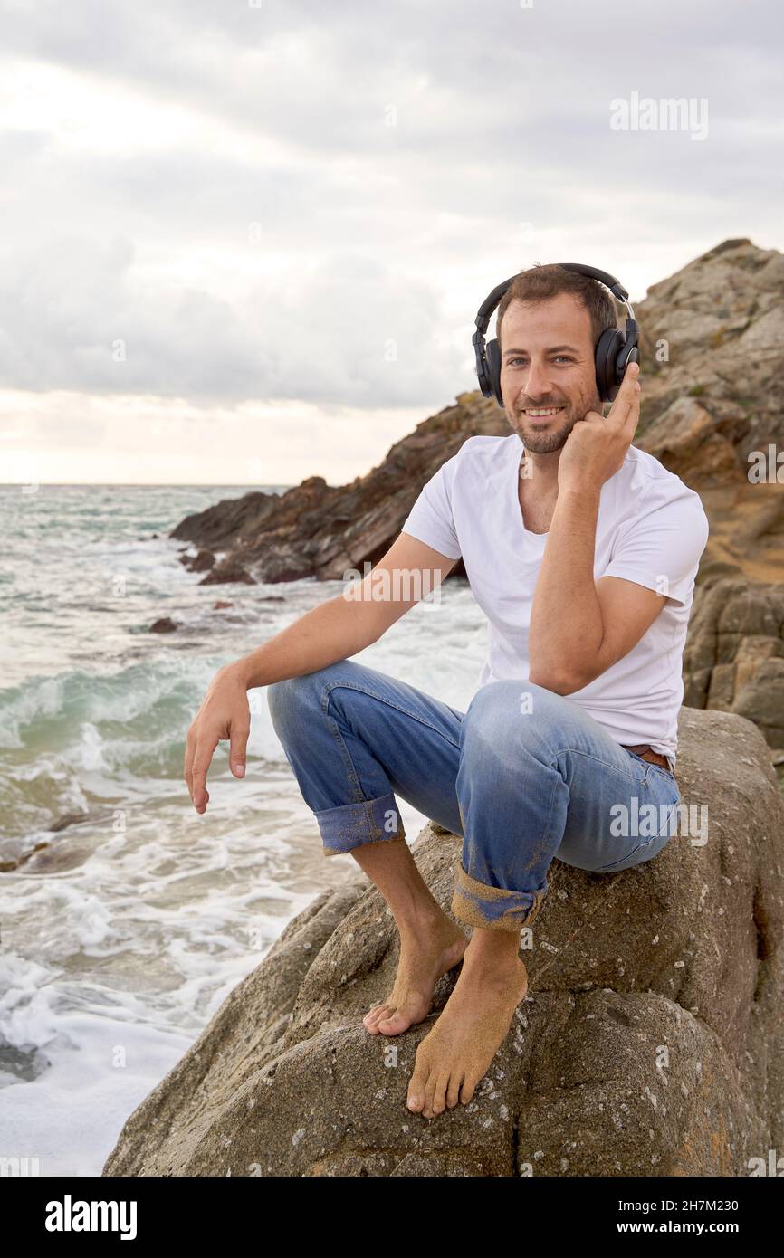 Smiling man listening music on headphones at beach Stock Photo