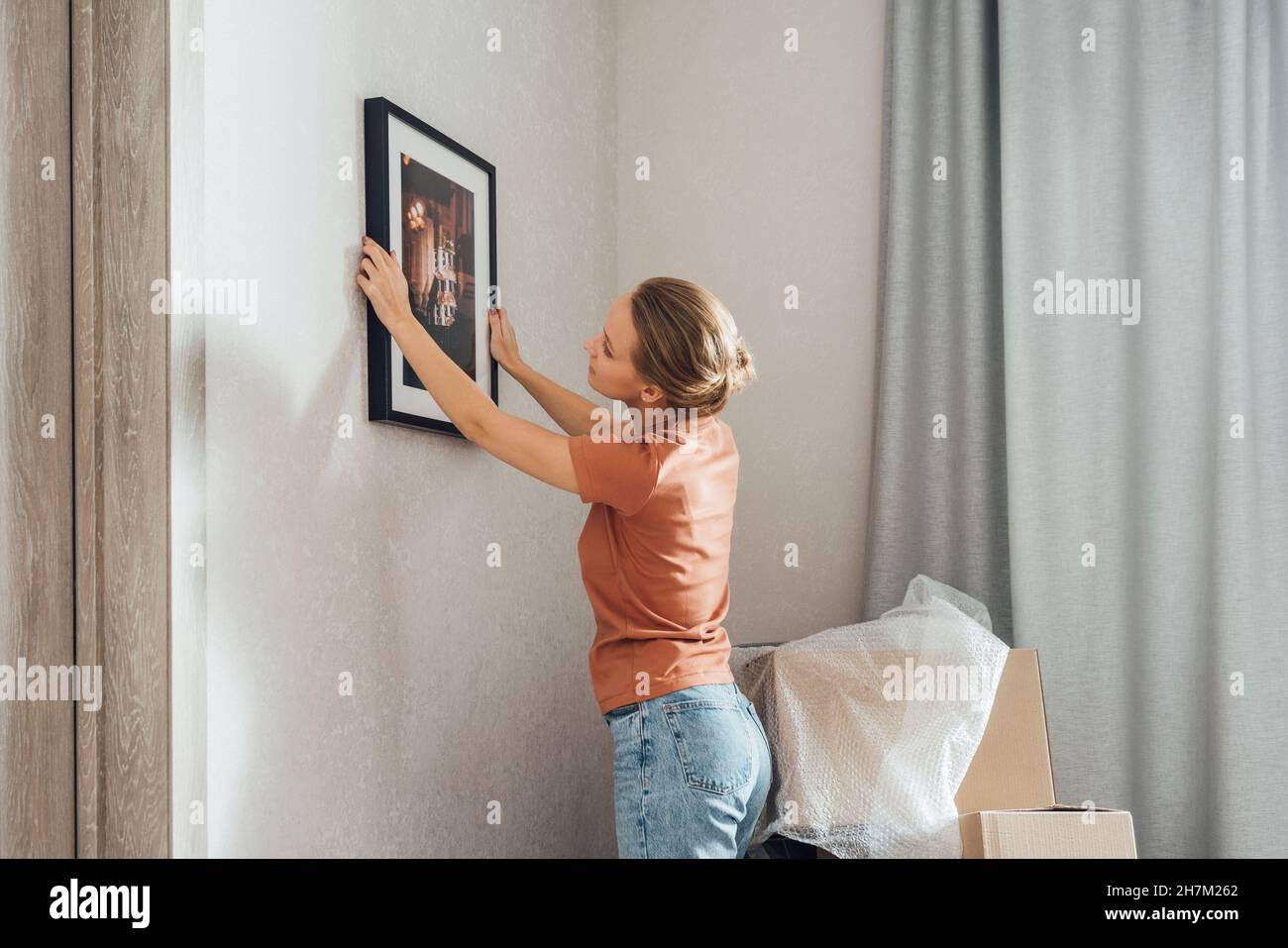 Young woman putting picture frame on wall at new home Stock Photo