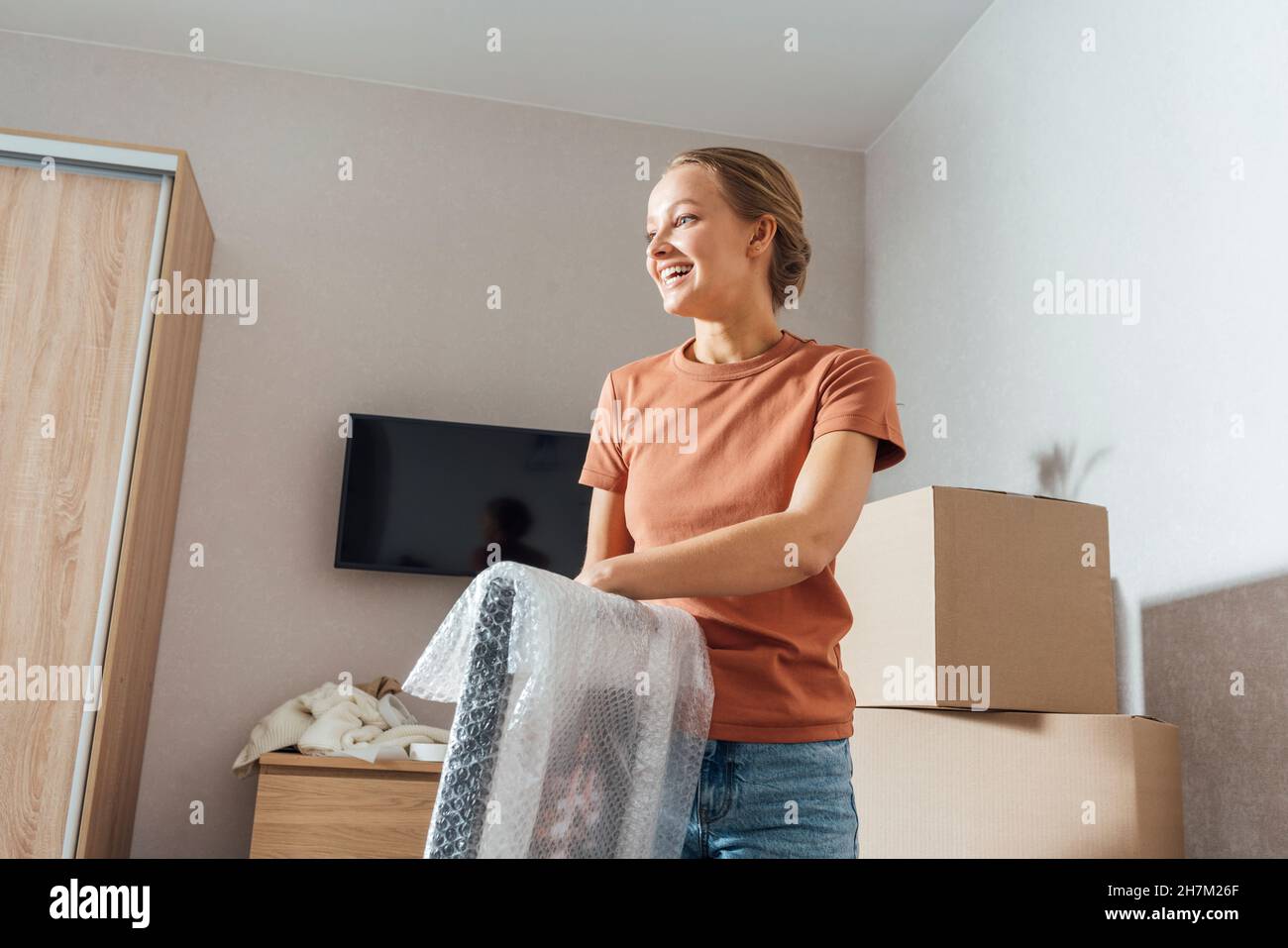 Smiling woman removing bubble wrap from picture frame at home Stock Photo