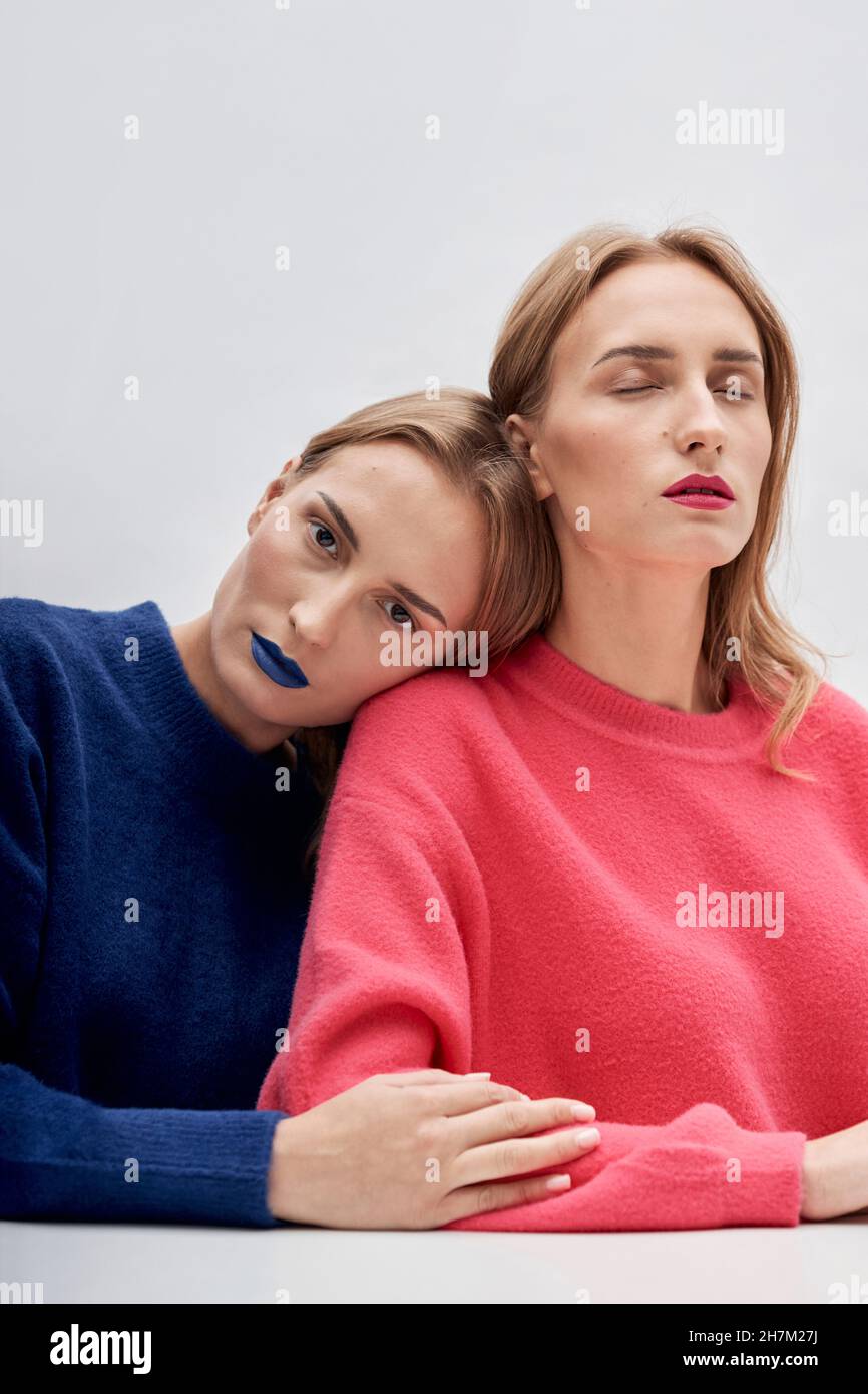 Woman with blue lipstick leaning on shoulder of twin sister against white background Stock Photo