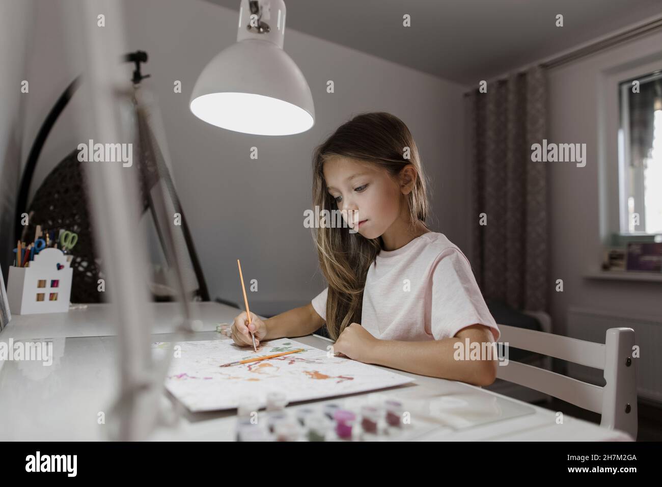 Girl painting on paper at desk Stock Photo