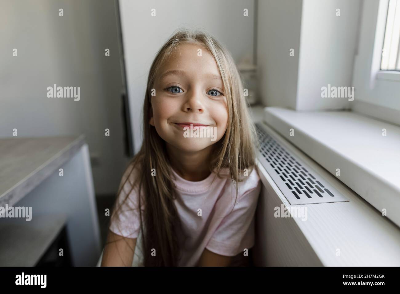 Smiling blond girl sitting at window Stock Photo