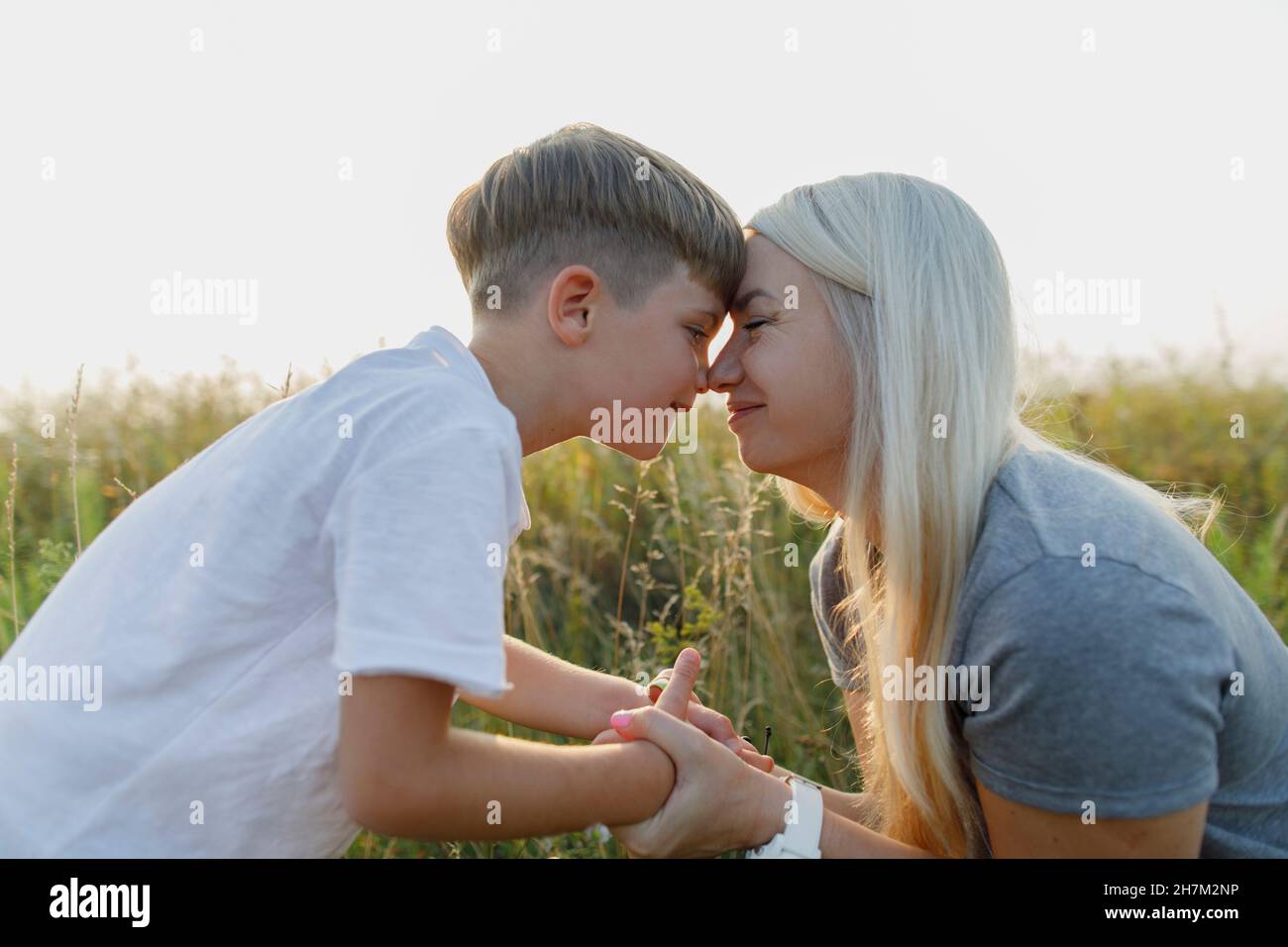 Mother and son face to face holding hands at meadow Stock Photo