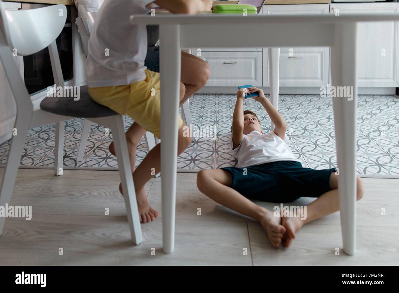 Boy using mobile phone under table lying on floor Stock Photo