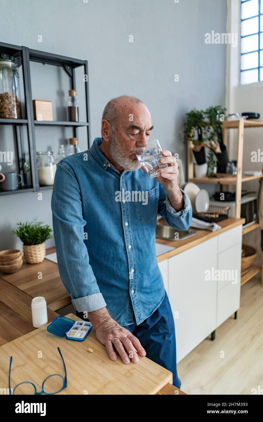 Thoughtful senior man taking medicine in kitchen at home Stock Photo