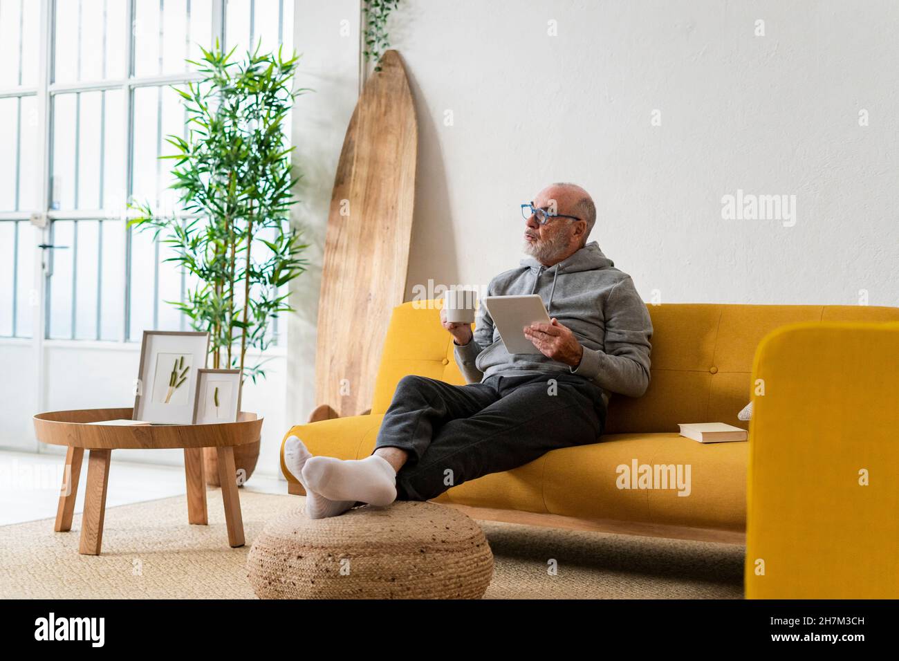 Man with coffee cup using tablet PC in living room Stock Photo