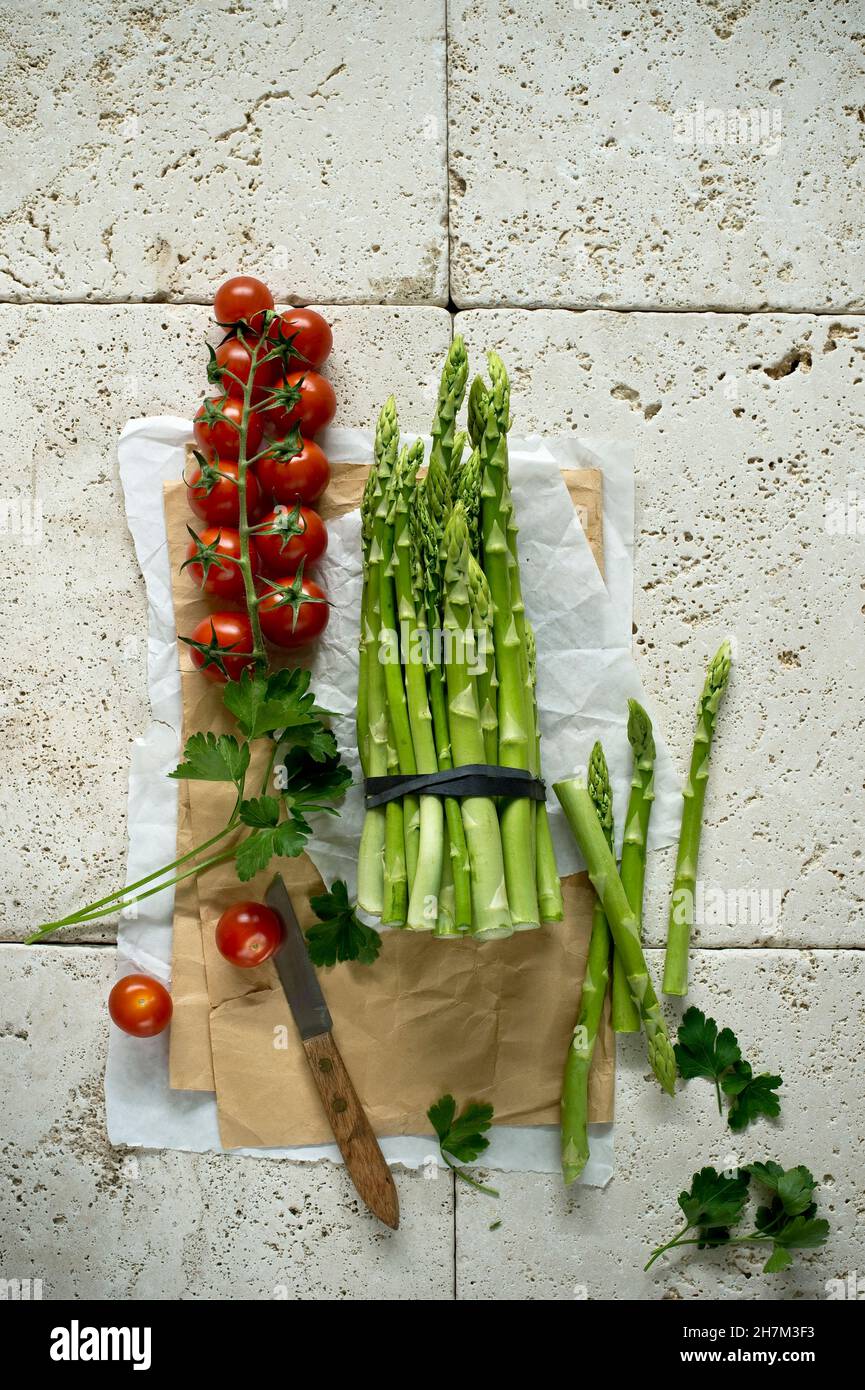 Studio shot of fresh tomatoes, parsley and asparagus bundle lying on stone surface Stock Photo