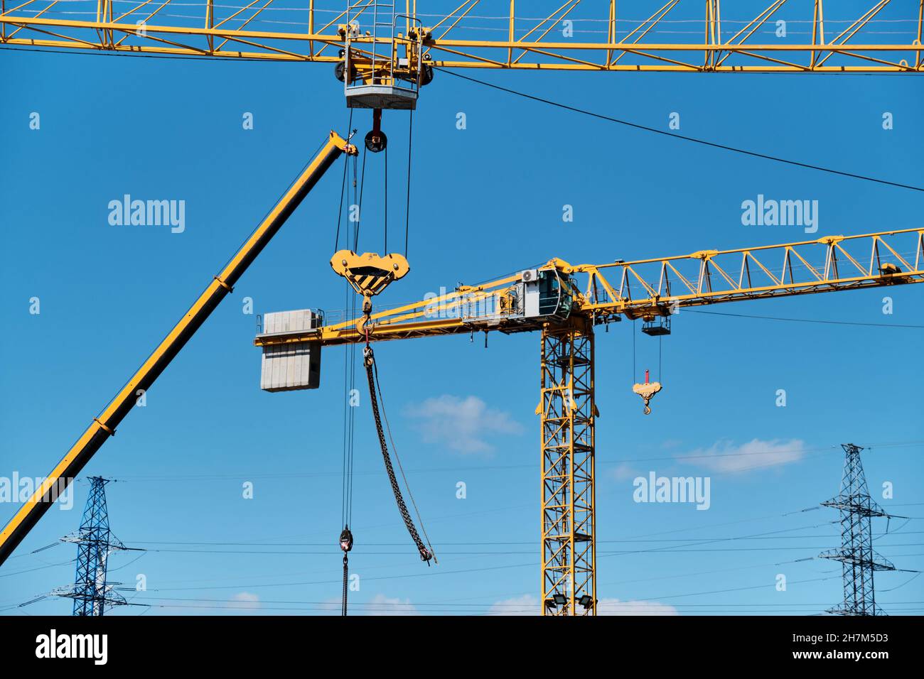 Several yellow construction cranes with hooks on chains Stock Photo - Alamy
