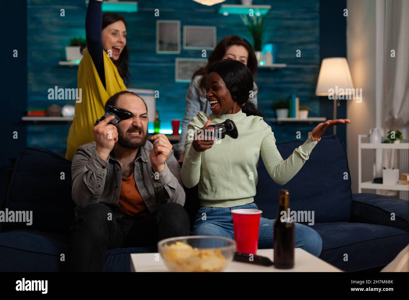 Upset nervous multiethnic friends holding controller playing video games losing online competition sitting on couch in front of tv. Group of people enjoying spending time together. Hanging out concept Stock Photo