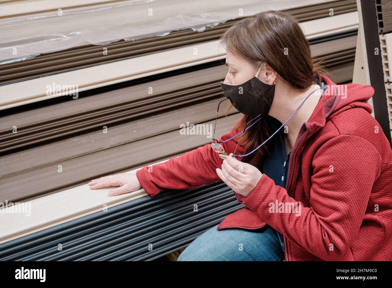 Woman in mask is located in store. She chooses paneling for the walls. Close up Stock Photo