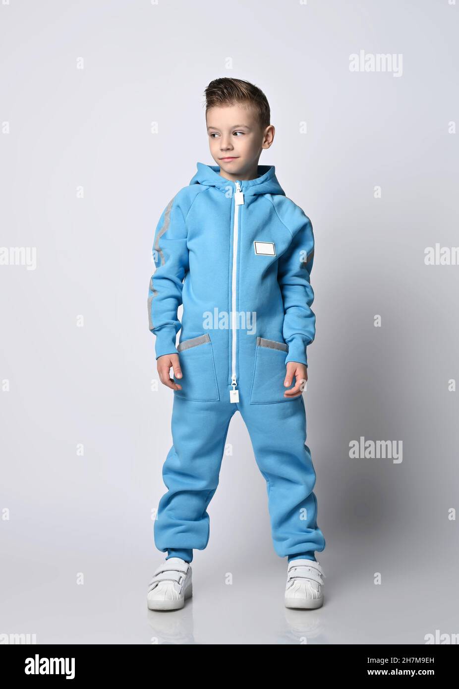 Calm, smart kid boy in blue jumpsuit with zipper and reflective stripes stands looking aside at copy space Stock Photo