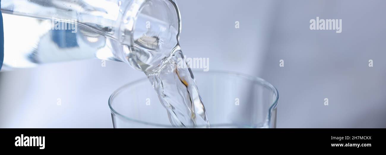 Scientist chemist pouring water from transparent bottle into flask in