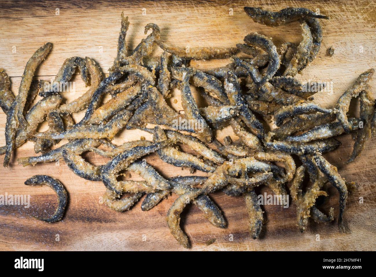 Fried and battered small Vendace fish (Coregonus albula) on a wooden cutboard Stock Photo