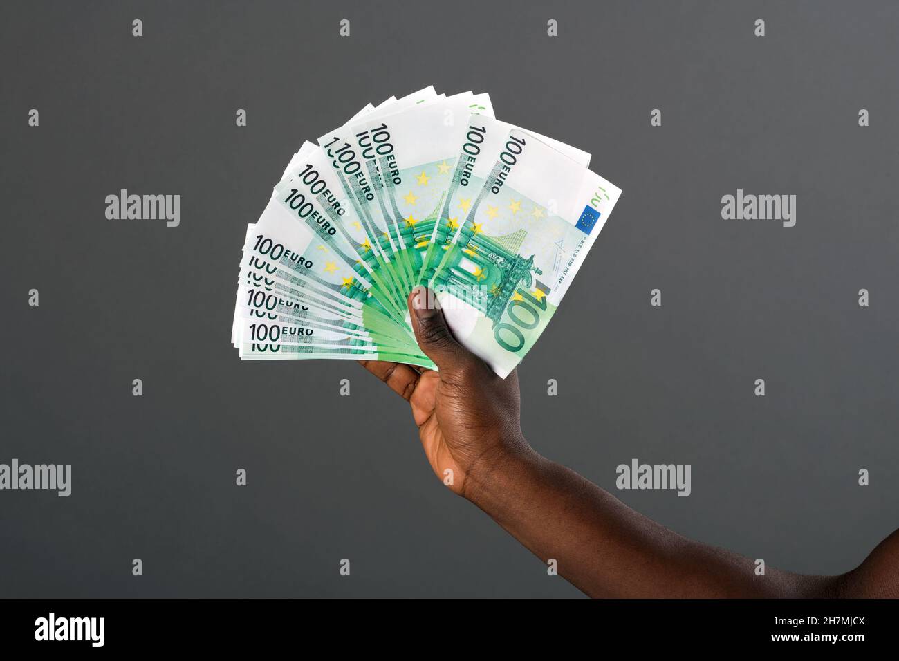 Black hand holding large fan of 100 Euro banknotes with a studio background. Stock Photo
